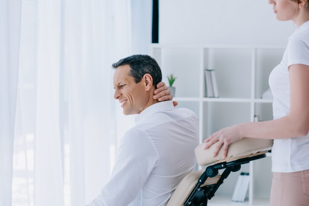 businessman with pain in neck sitting in masseuse office