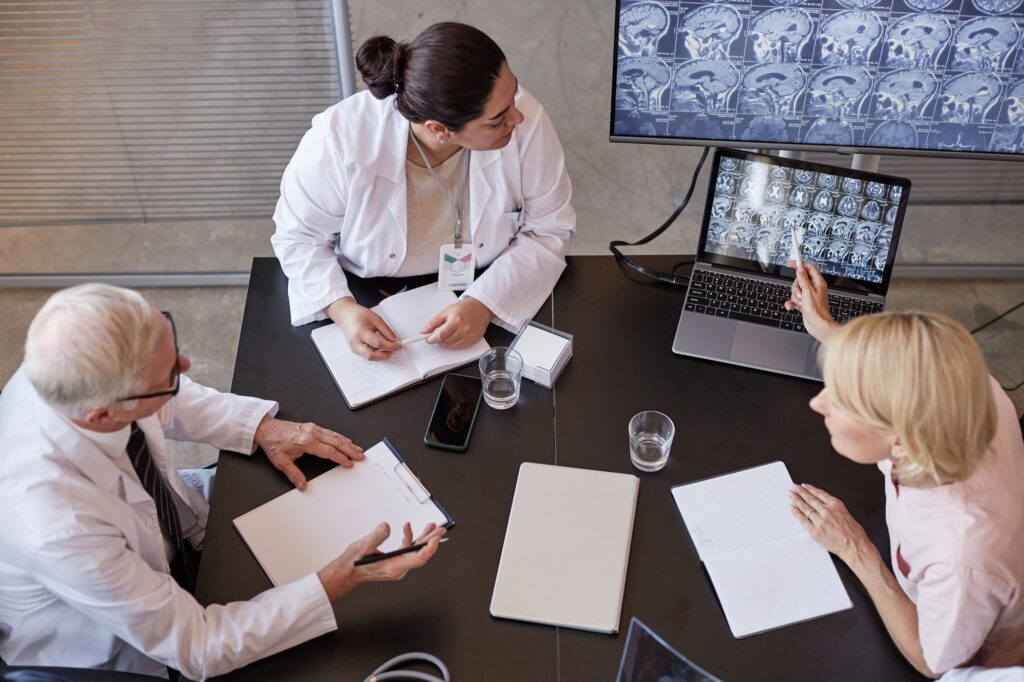Female Neurosurgeon Discussing X Ray Imaging with Colleagues Pointing at Screen at Table