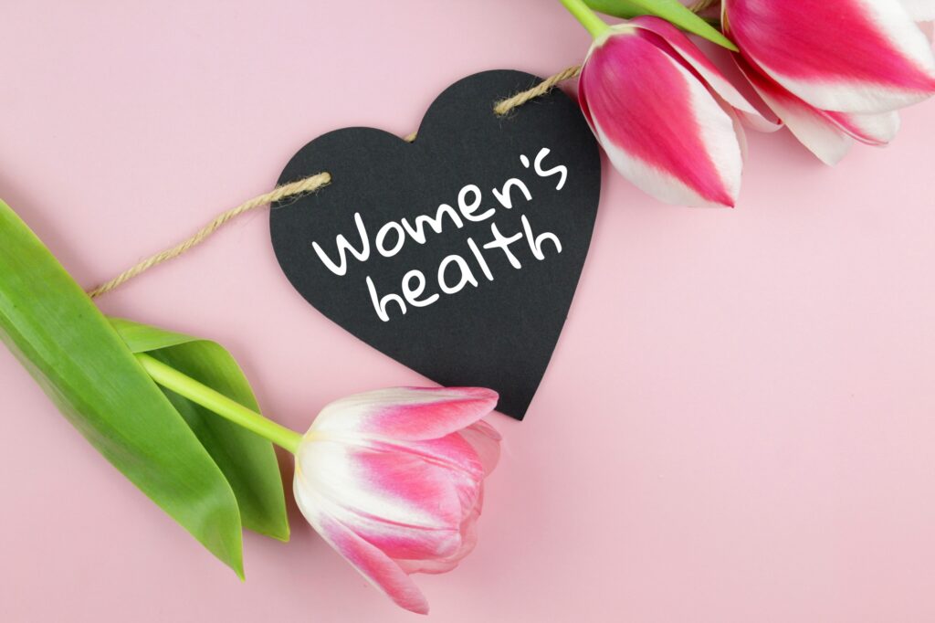 heart with the inscription women’s health hanging on a rope and tulips on a pink background